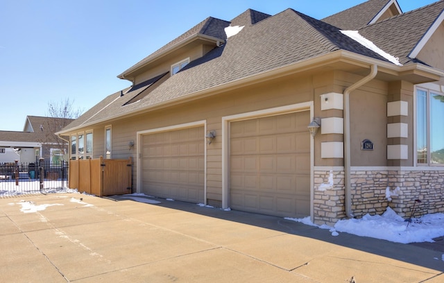 view of property exterior with a garage, a shingled roof, fence, stone siding, and driveway