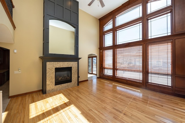 unfurnished living room featuring light wood-style floors, a glass covered fireplace, a wealth of natural light, and a towering ceiling