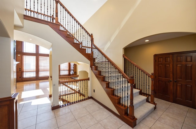 stairway featuring baseboards, arched walkways, a towering ceiling, and tile patterned floors