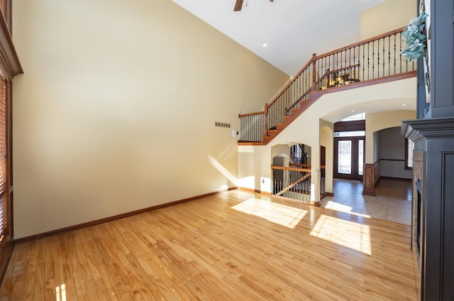 unfurnished living room featuring visible vents, arched walkways, baseboards, hardwood / wood-style flooring, and a high ceiling