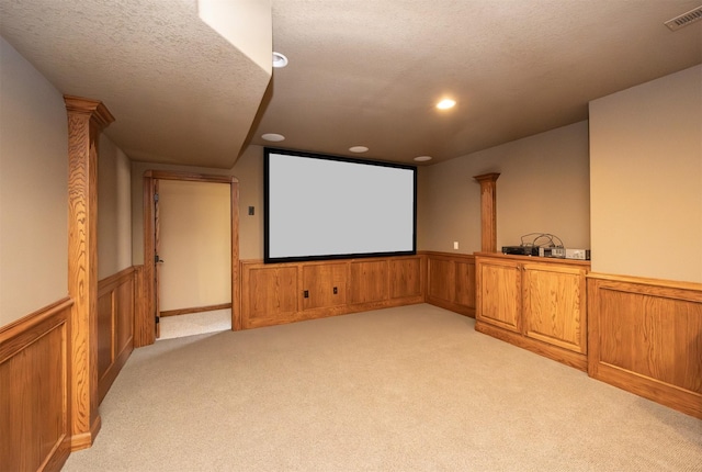 cinema room with light carpet, wainscoting, visible vents, and a textured ceiling