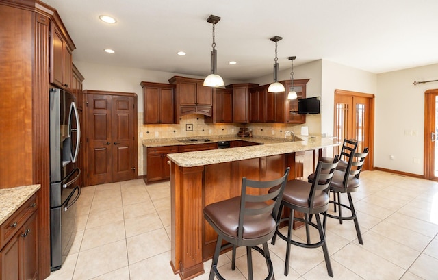 kitchen with stainless steel refrigerator with ice dispenser, backsplash, light tile patterned flooring, light stone countertops, and a kitchen breakfast bar