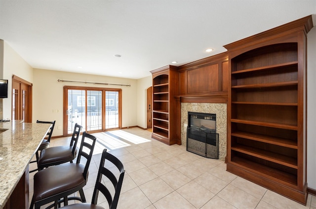 living area featuring light tile patterned floors, recessed lighting, a glass covered fireplace, and baseboards