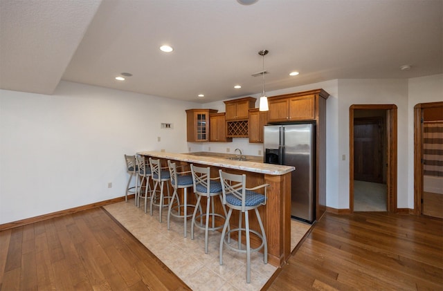 kitchen featuring a kitchen breakfast bar, stainless steel refrigerator with ice dispenser, wood finished floors, and brown cabinets