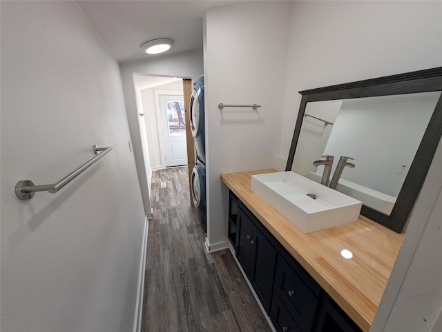 bathroom featuring vanity, baseboards, stacked washer / dryer, and wood finished floors