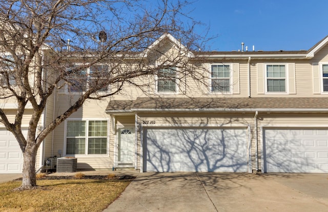 view of property with driveway, an attached garage, central AC unit, and roof with shingles