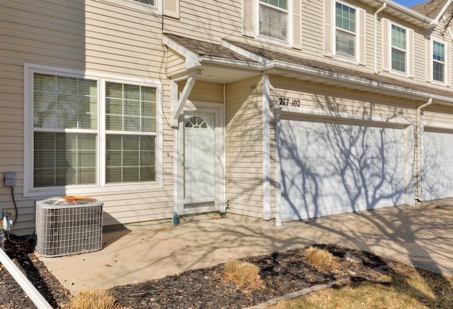 doorway to property with a garage, central AC, and roof with shingles