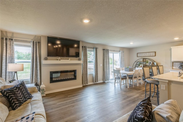 living area featuring a textured ceiling, recessed lighting, wood finished floors, baseboards, and a glass covered fireplace