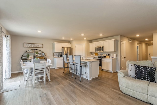 kitchen featuring light wood-style flooring, stainless steel appliances, visible vents, white cabinetry, and open floor plan