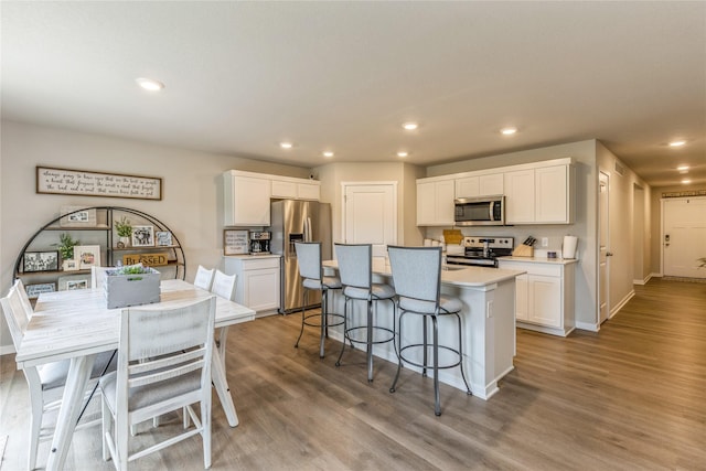 kitchen featuring wood finished floors, white cabinets, appliances with stainless steel finishes, a kitchen bar, and a center island with sink