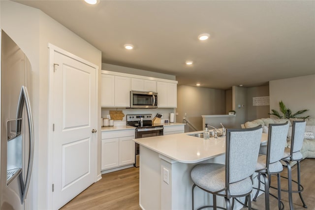 kitchen featuring a center island with sink, stainless steel appliances, light wood-style floors, a kitchen bar, and a sink