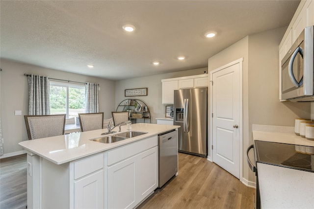 kitchen featuring white cabinets, appliances with stainless steel finishes, a kitchen island with sink, light countertops, and a sink