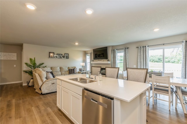 kitchen featuring stainless steel dishwasher, open floor plan, white cabinets, a sink, and light wood-type flooring