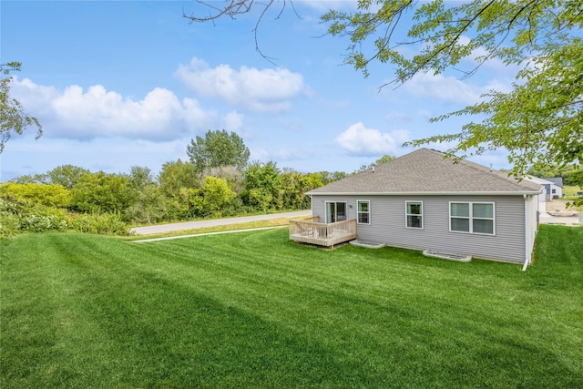 rear view of house with a deck, a lawn, and roof with shingles