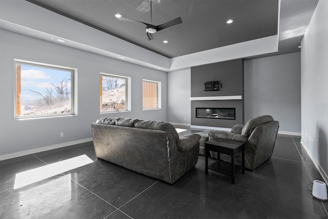 living room with recessed lighting, baseboards, a raised ceiling, and a glass covered fireplace