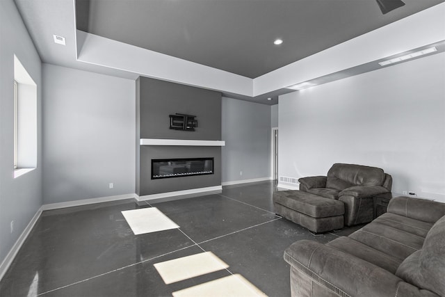 living room featuring a glass covered fireplace, a tray ceiling, finished concrete flooring, and baseboards