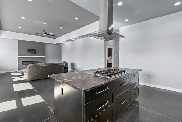 kitchen featuring recessed lighting, stainless steel gas cooktop, island range hood, a ceiling fan, and a glass covered fireplace