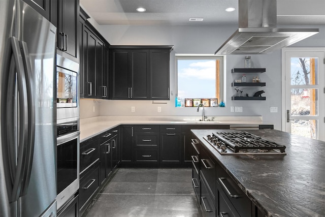 kitchen featuring appliances with stainless steel finishes, dark cabinetry, island exhaust hood, and a sink