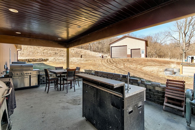 view of patio with exterior kitchen, outdoor dining space, a grill, and an outdoor structure