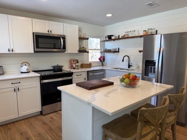 kitchen with open shelves, stainless steel appliances, white cabinetry, a sink, and a kitchen breakfast bar