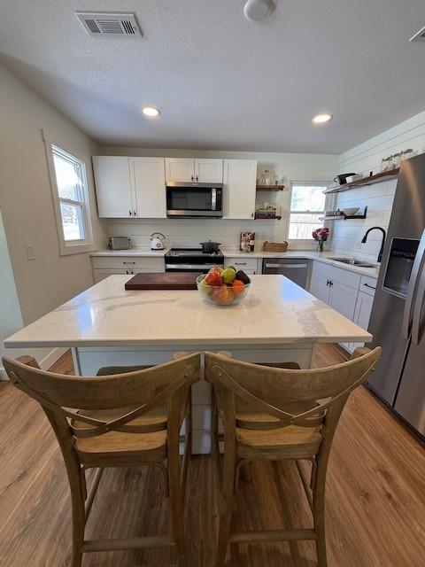 kitchen featuring visible vents, wood finished floors, stainless steel appliances, open shelves, and a sink