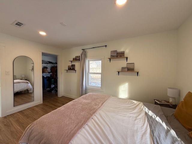 bedroom with baseboards, visible vents, wood finished floors, a walk in closet, and recessed lighting