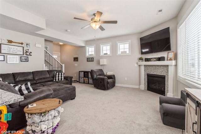 carpeted living area featuring ceiling fan, visible vents, baseboards, stairway, and a glass covered fireplace