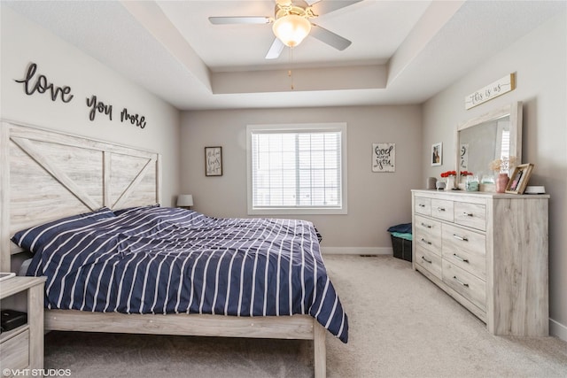 bedroom featuring a ceiling fan, a raised ceiling, light colored carpet, and baseboards