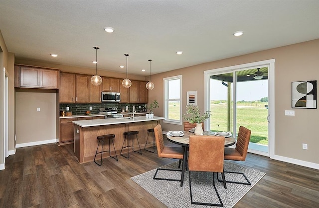 kitchen with brown cabinets, dark wood finished floors, stainless steel appliances, light countertops, and backsplash