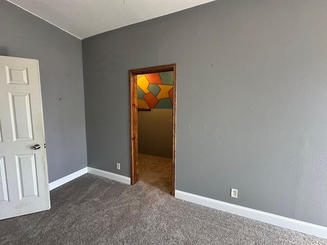 spare room featuring dark carpet and baseboards