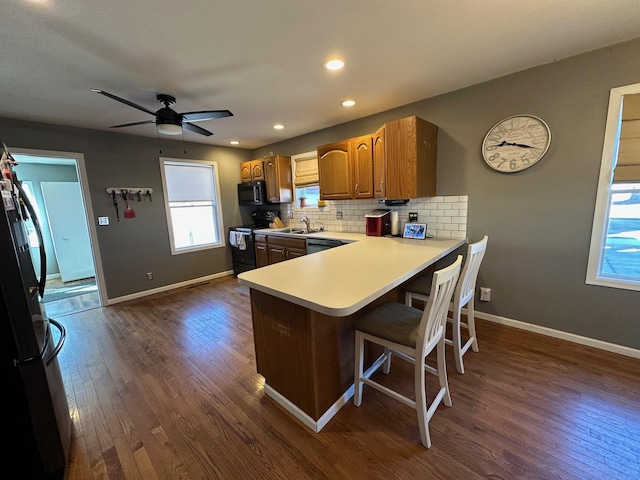 kitchen featuring baseboards, dark wood finished floors, a peninsula, black appliances, and backsplash