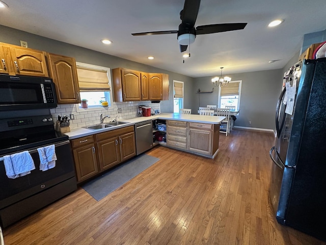 kitchen featuring tasteful backsplash, wood finished floors, a peninsula, black appliances, and a sink