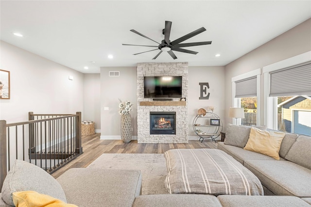 living room with recessed lighting, visible vents, a stone fireplace, wood finished floors, and baseboards