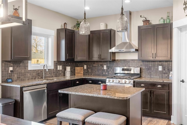 kitchen with dark brown cabinetry, a sink, appliances with stainless steel finishes, backsplash, and wall chimney exhaust hood