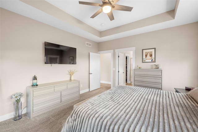 carpeted bedroom featuring a tray ceiling, visible vents, ceiling fan, and baseboards