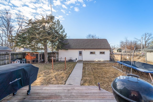 rear view of house with a deck, a fenced backyard, a yard, roof with shingles, and a trampoline