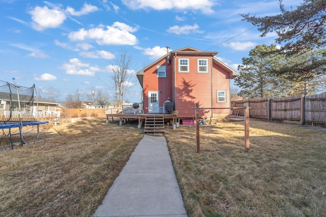 back of house featuring a fenced backyard, a trampoline, a lawn, and a wooden deck