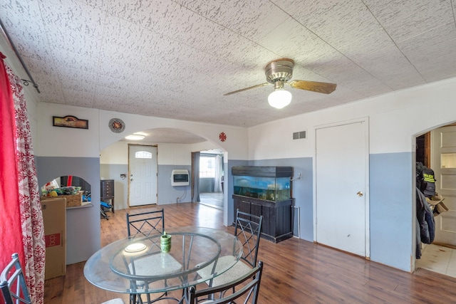 dining room featuring visible vents, arched walkways, a ceiling fan, wood finished floors, and heating unit