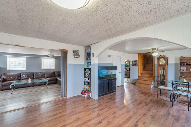 living room with arched walkways, wood finished floors, visible vents, a ceiling fan, and stairs