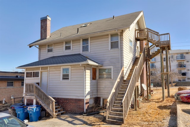 rear view of property with stairs, a shingled roof, and a chimney