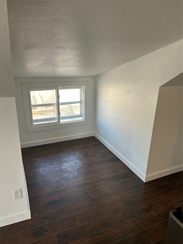 unfurnished room with dark wood-type flooring, a textured wall, a textured ceiling, and baseboards