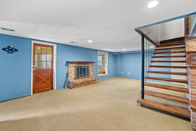 unfurnished living room with stairway, a brick fireplace, carpet, and visible vents