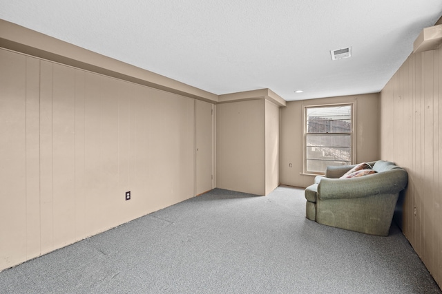 unfurnished room featuring light colored carpet, visible vents, wood walls, and a textured ceiling