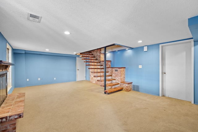 finished below grade area with a glass covered fireplace, carpet flooring, visible vents, and a textured ceiling