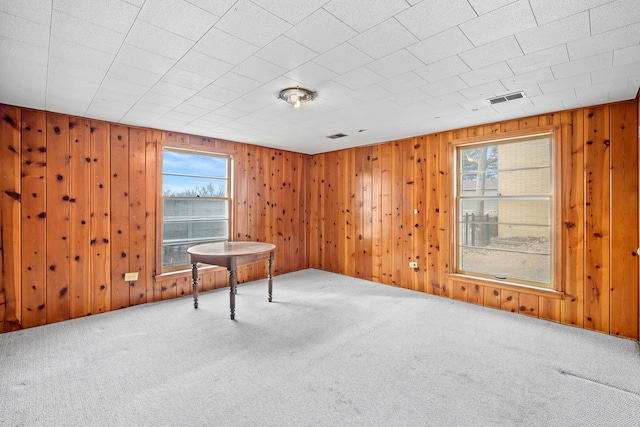 spare room featuring wooden walls, carpet flooring, visible vents, and a wealth of natural light