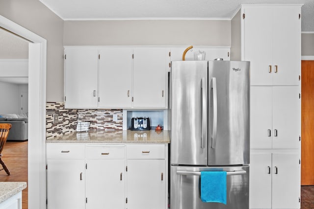 kitchen with backsplash, wood finished floors, white cabinetry, freestanding refrigerator, and crown molding