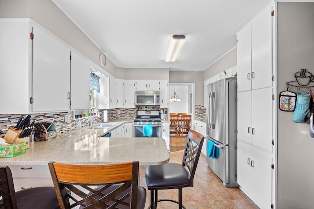 kitchen featuring a sink, a kitchen breakfast bar, stainless steel appliances, a peninsula, and decorative backsplash