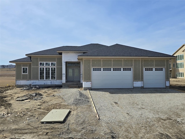 view of front of house with stucco siding, an attached garage, dirt driveway, and a shingled roof