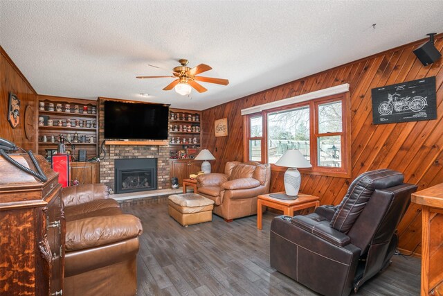 living area featuring a textured ceiling, wood walls, a brick fireplace, and wood finished floors