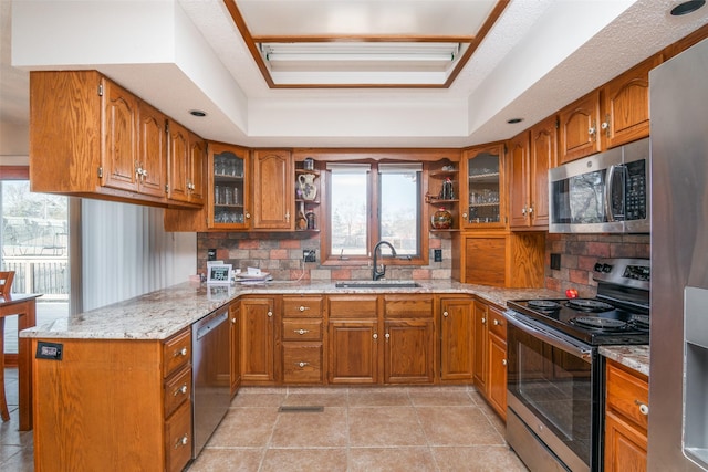 kitchen with brown cabinetry, a tray ceiling, stainless steel appliances, and a sink